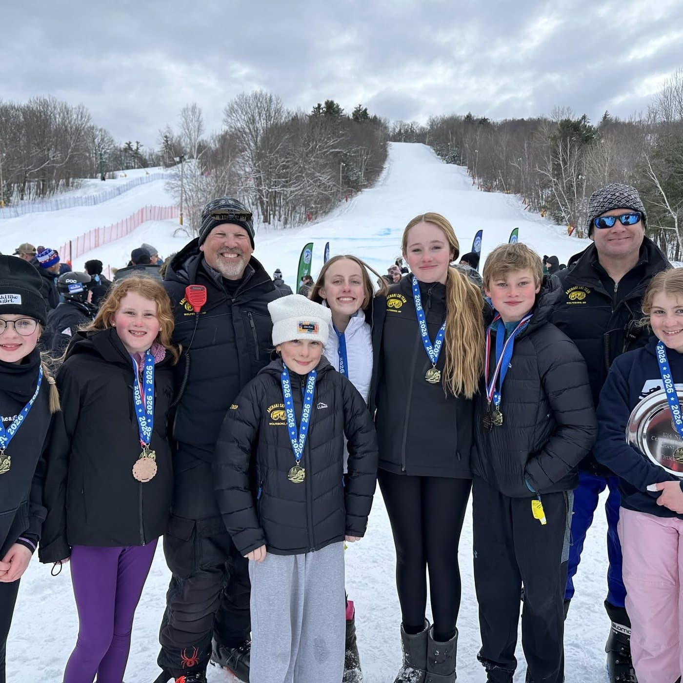 Abenaki athletes and coaches with medals and a trophy at the bottom of the hill