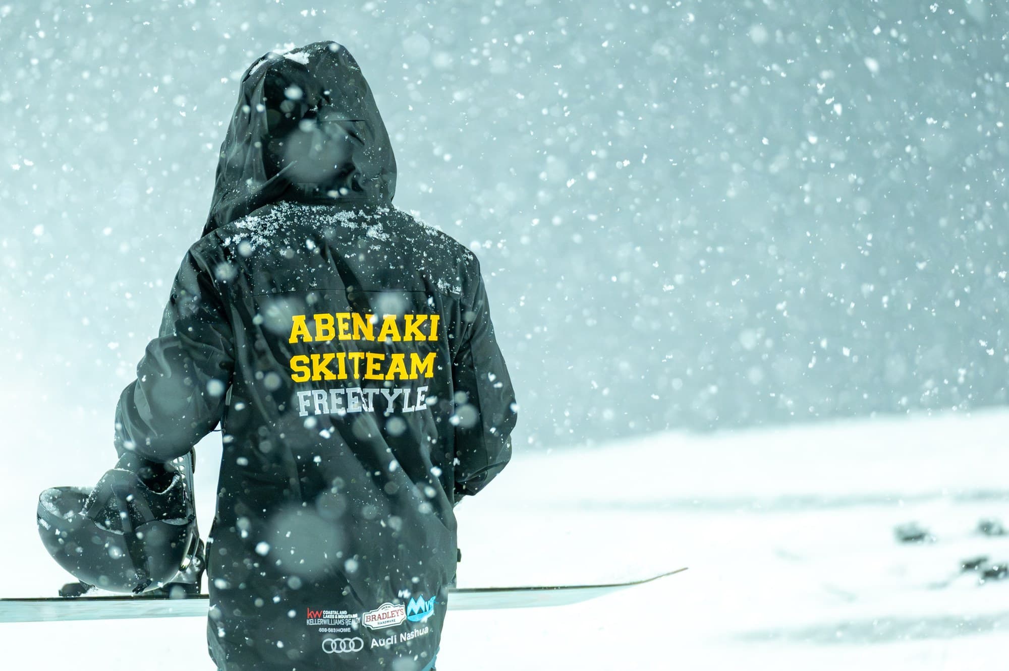 The back of a coach's jacket reading Abenaki Ski Team Freestyle, in heavy snow at the top of the park
