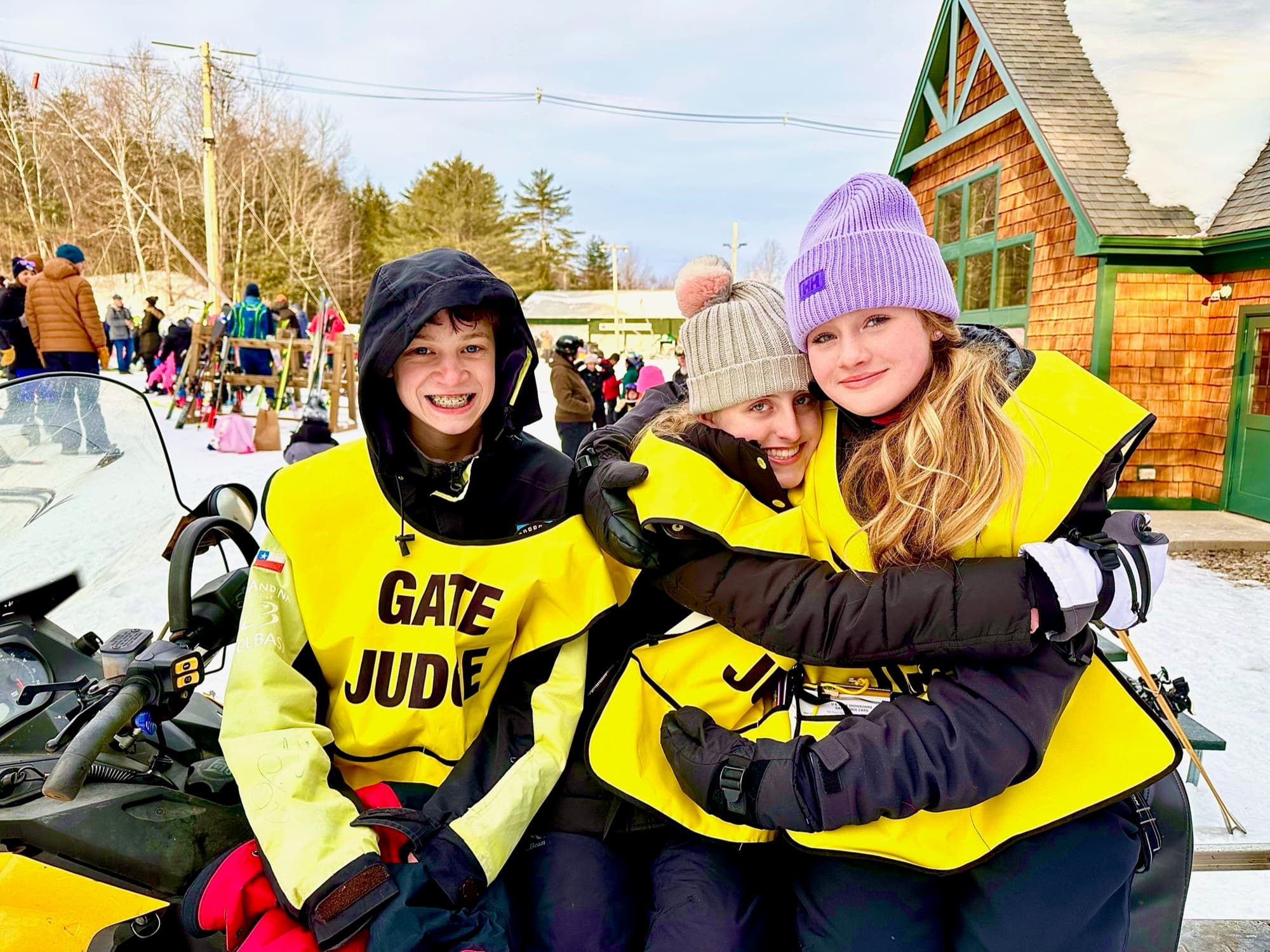 Three gate judges in yellow vests on a snowmobile outside the lodge on race day