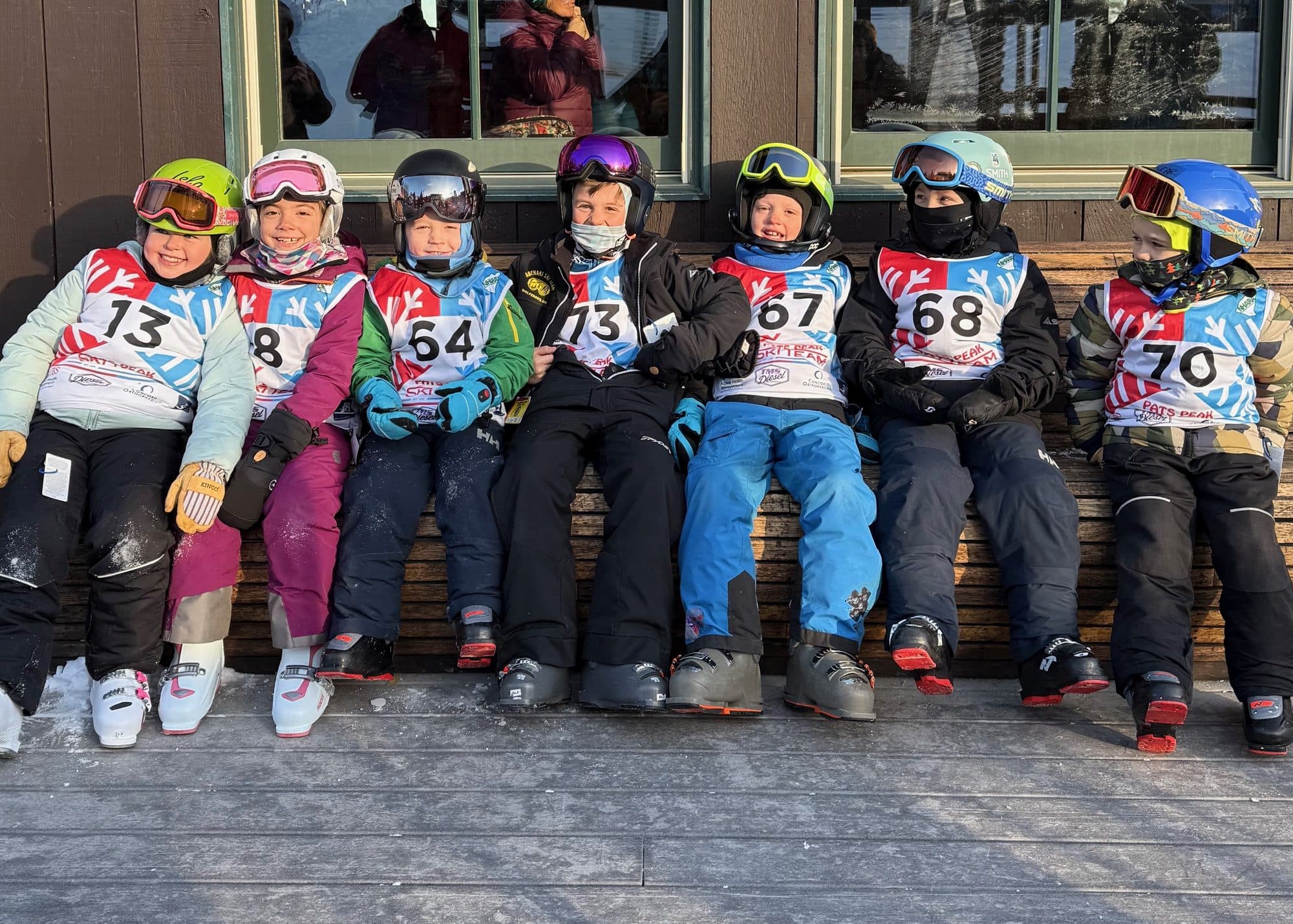 U8 racers in bibs sitting together outside the lodge on race day