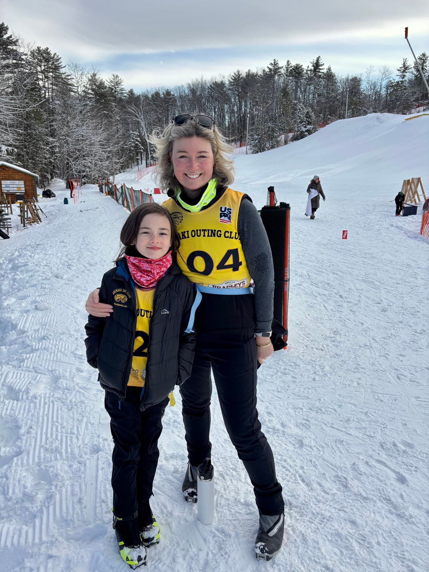 A volunteer in an Abenaki Outing Club bib with an arm around a young skier at the base of the hill