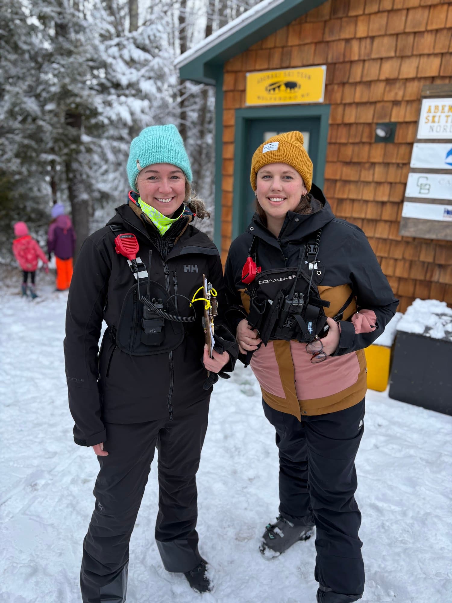 Two race officials with radios and a clipboard outside the Abenaki Ski Team hut