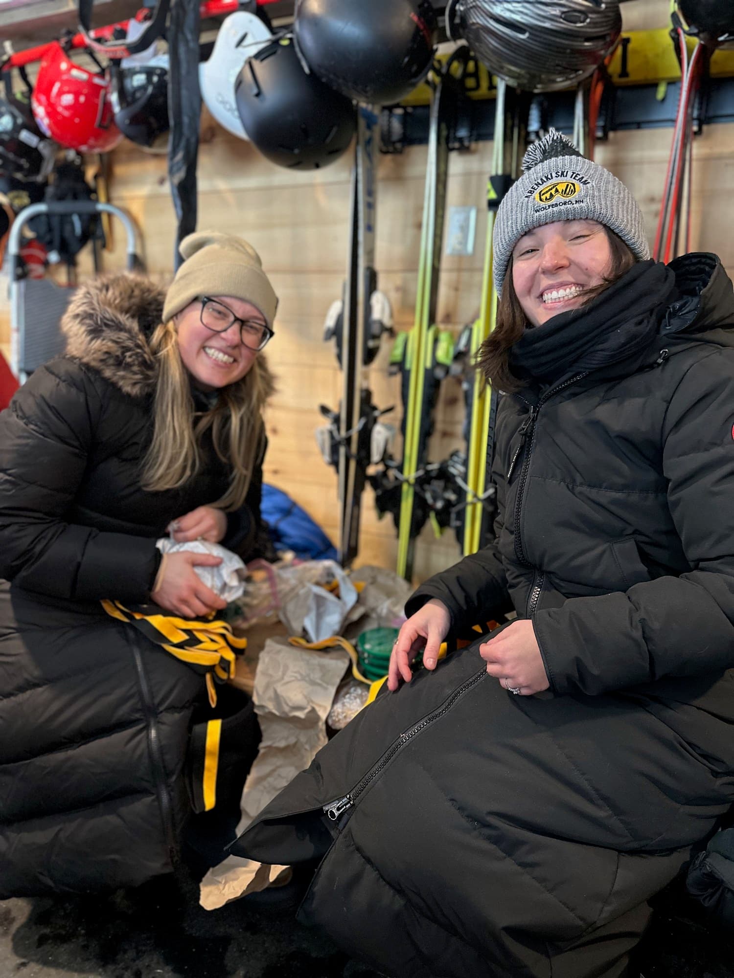 Two volunteers sorting bibs in the equipment room under the helmet rack