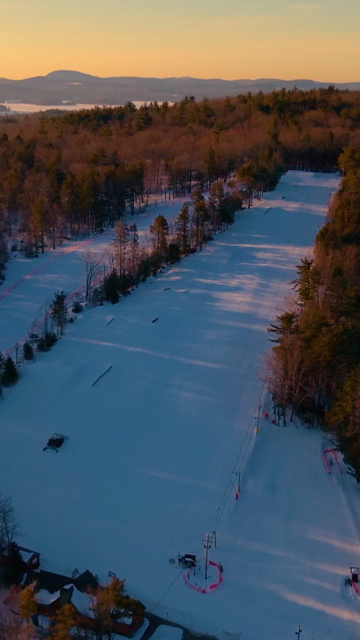 Drone footage over Abenaki Ski Area at sunset: the groomed trails, the rope tow and the lodge, with the lake and mountains beyond