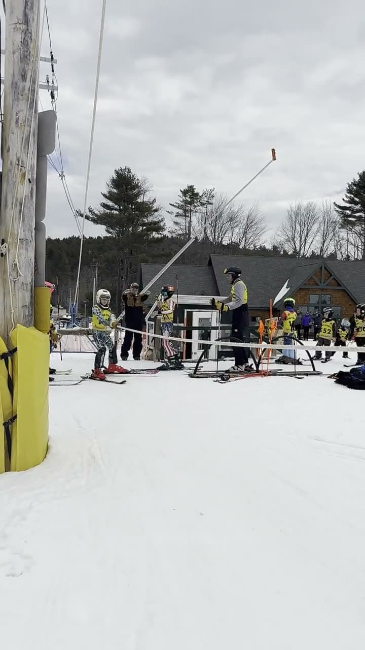A race day at Abenaki from the tow to the finish line: a young racer riding the rope tow up past the tower, two carves through the gates, a racer crossing the blue finish line past the camera, and the U8 group coming down the hill together