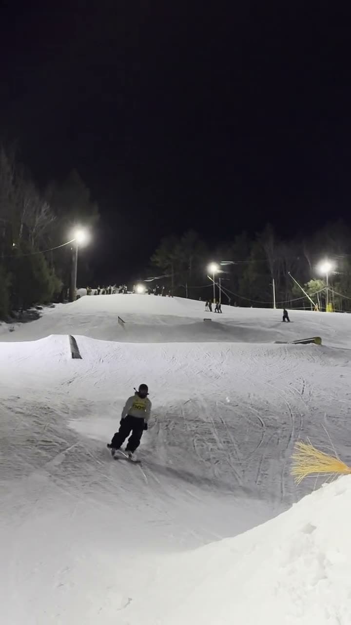 A Monday night in the terrain park: a skier dropping in under the lights, a grab off the jump, a full flip with the crowd along the lip, a backflip, and the ride-out toward the lodge